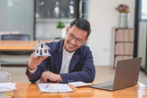 Accountant, businessman, real estate agent, businessman handing model house to customers along with house interest calculation documents for customers to sign. photo