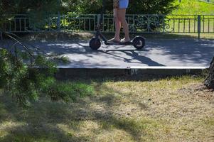 una niña monta un nuevo scooter eléctrico moderno de dos ruedas de pie con dos pies en un scooter eléctrico en la carretera en el parque contra el telón de fondo de los árboles y la naturaleza foto