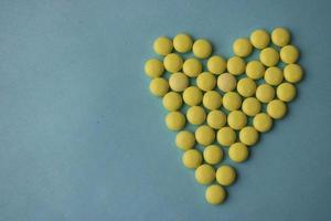 Small medical pharmaceptic round yellow pills, vitamins, drugs, antibiotics in the form of a heart on a blue background, texture. Concept medicine, health care, heart disease. Flat lay, top view photo