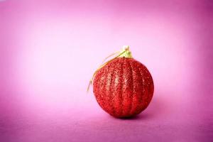 Red small round glass plastic winter smart shiny decorative beautiful xmas festive Christmas ball, Christmas toy plastered over sparkles on a pink purple background photo