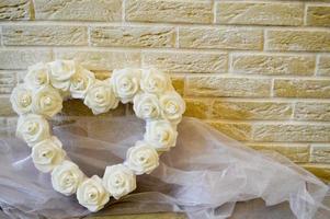 corazón blanco con rosas blancas y diamantes. fondo de ladrillos beige. tela blanca transparente. foto