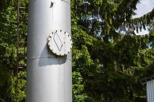 Large iron metal stainless brilliant industrial tank column with a folding round hatch, manhole with bolts, nuts and studs against the background of green trees and woods photo