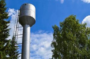 gran torre de agua industrial de acero inoxidable brillante para suministrar agua de gran capacidad, barril contra el cielo azul y los árboles foto