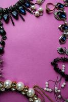 Beautiful precious shiny jewelery trendy glamorous jewelry set, necklace, earrings, rings, chains, brooches with pearls and diamonds on a pink purple background. Flat lay, top view, copy place photo