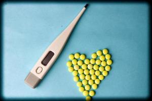 Small medical pharmaceptic round pills, vitamins, drugs in the form of a heart and electronic thermometer on a blue background. Concept medicine, health care, heart disease. Flat lay, top view photo