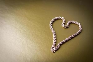 Texture of a beautiful golden festive chain unique weaving in the shape of a heart on a yellow gold background and copy space. Concept love, marriage proposal, marriage, St. Valentine's Day photo