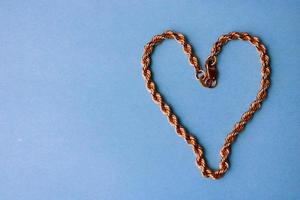 Texture of a beautiful golden dear festive chain of unique weaving in the shape of a heart on a blue background and copy space. Concept love, marriage proposal, marriage, St. Valentine's Day photo