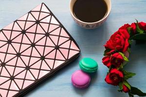 Cosmetic bag, cup of coffee, roses and macaroons on blue background photo