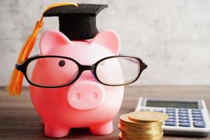 Pigging bank wearing eyeglass with coins and calculator saving bank education concept. photo