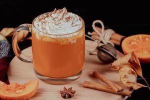 Pumpkin coffee latte with whipped cream on dark background. Hot autumn drink with cinnamon and spices in glass mug on a wooden tray. photo