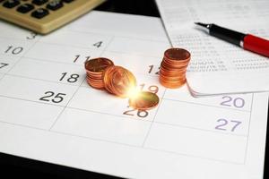 filas de monedas sobre calendario con librero y calcutor foto