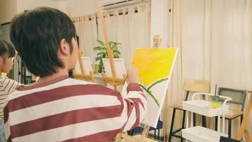 un garçon asiatique talentueux concentre des leçons de compétences sur la peinture acrylique couleur sur toile dans une salle de classe d'art et apprend de manière créative avec une enseignante à l'école primaire. video