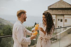 pareja joven relajándose en la terraza al aire libre y bebiendo jugo de naranja fresco