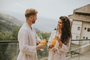 pareja joven relajándose en la terraza al aire libre y bebiendo jugo de naranja fresco