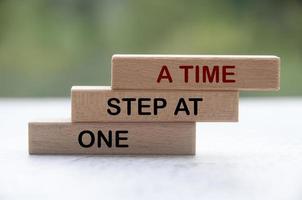 One step at a time words on wooden blocks with blurred nature background. Work completion concept. photo