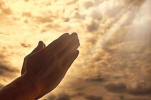 Hand praying with bright shining light on sky background. Religious and spiritual concept photo