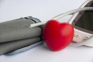 Digital blood pressure monitor and heart shape on white background photo