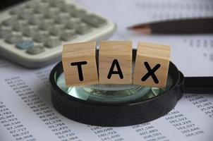 Tax word labeled wooden blocks on magnifying glass. Tax investigation concept.calculator and number analysis background. Tax concept photo