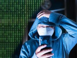 Asian man in hoodie and mask hacking Something from a mobile phone intended for blurry photos has digital numbers. number one with zero