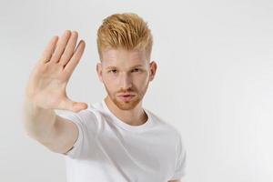 Stop hands sign. Young man in blank template white t shirt showing stop gesture. Redheaded and red beard guy isolated. hazard protection concept. Copy space and mock up on t-shirt. Selective focus photo