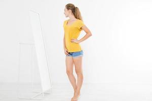 Shopping sale concept. Blonde girl in jeans and t shirt. Young woman in good body shape looking at mirror and lose weight. Copy space photo