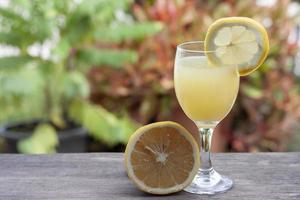 limonada en vidrio y trozos de limones en rodajas sobre una mesa de madera y desenfoque de fondo de la naturaleza. foto