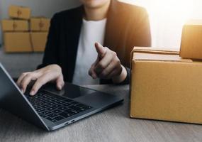 joven y atractiva mujer asiática propietaria de un negocio de inicio mira el trabajo de la cámara feliz con la caja en casa prepara la entrega de paquetes en la cadena de suministro de pymes, adquisiciones, omnicanal o concepto de cuarentena de coronavirus. foto