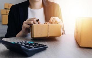 joven y atractiva mujer asiática propietaria de un negocio de inicio mira el trabajo de la cámara feliz con la caja en casa prepara la entrega de paquetes en la cadena de suministro de pymes, adquisiciones, omnicanal o concepto de cuarentena de coronavirus. foto