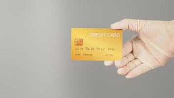 la mano sostiene una tarjeta de crédito dorada sobre fondo gris. la mano lleva un guante médico blanco. foto