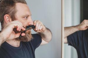 Man cutting moustache and beard himself at home photo