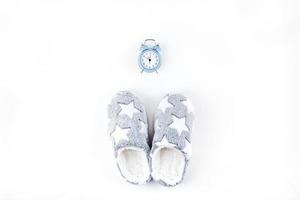 Soft fluffy slippers and blue alarm clock photo