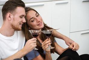 jóvenes y mujeres divirtiéndose y bebiendo cócteles mientras se sientan en el piso de la cocina en casa foto