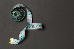 Top view of measure tape curtailed into a spiral with copy space. Concept of sewing accessory or healthy diet on black background photo