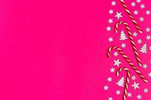 bastón de caramelo de navidad mintió uniformemente en fila sobre fondo rosa con copo de nieve decorativo y estrella. plano y vista superior foto