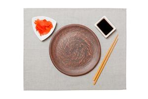 Empty round brown plate with chopsticks for sushi, ginger and soy sauce on grey napkin background. Top view with copy space for you design photo