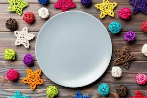 Top view of holiday plate decorated with knitted baubles and stars on wooden background. New Year decorations and toys. Family Christmas dinner concept photo