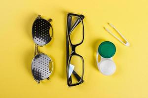 A set of accessories for sight. Pinhole glasses, lenses with container and glasses for sight. Pair of medical pinhole glasses with reflections. Medical concept. Top view photo