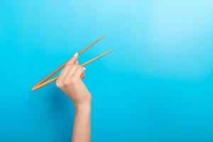 Girl's hand showing chopsticks on blue background. Asian cuisine concept with empty space for your design photo