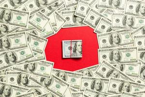 marco de billetes de cien dólares con pila de dinero en el medio. vista superior del concepto de negocio sobre fondo rojo con espacio de copia foto