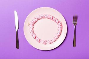 Measuring tape in a plate with fork and knife on both sides on purple background. Top view of weight loss concept photo