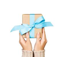 Woman hands give wrapped valentine or other holiday handmade present in paper with blue ribbon. Present box, decoration of gift Isolated on white photo