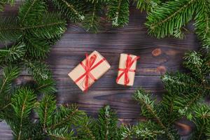 Christmas presents with red ribbon on dark wooden background in a frame made of fir branches with canes. Flat lay style photo