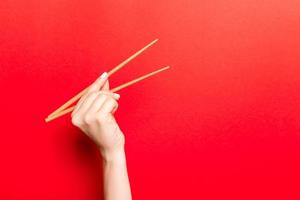 Creative image of wooden chopsticks in female hand on red background. Japanese and chinese food with copy space photo