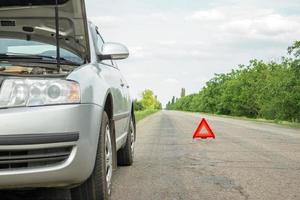 señal roja de parada de emergencia y coche plateado roto en la carretera foto