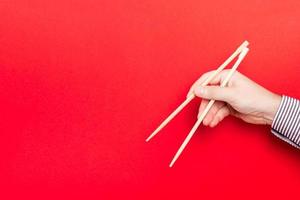 Wooden chopsticks holded with male hands on red background. Ready for eating concepts with empty space photo