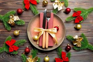 Top view of New Year dinner on festive wooden background. Composition of plate, fork, knife, fir tree and decorations. Merry Christmas concept photo