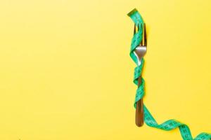 Fork is wrapped in measuring tape on yellow background with top view. Concept of diet for weight loss photo