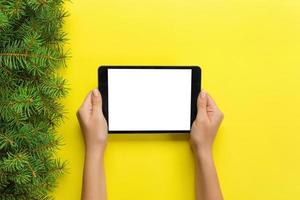 female hands with tablet computer on yellow christmas background. Xmas tree branch top view photo