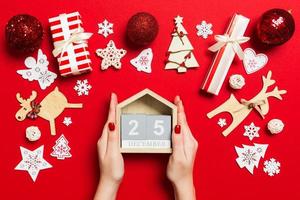 Top view of female hands holding calendar on red background. The twenty fifth of December. Holiday decorations. Christmas time concept photo