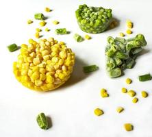 Frozen vegetables close-up on a white background Frozen corn, green peas, chopped green beans photo